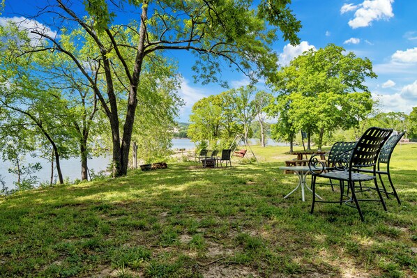 Un área de picnic junto al lago con una mesa y sillas, rodeada de árboles y vista al agua.