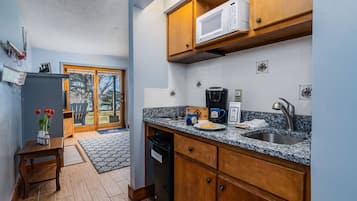 A compact kitchen with wooden cabinets, a microwave, a coffee maker, and a sink.