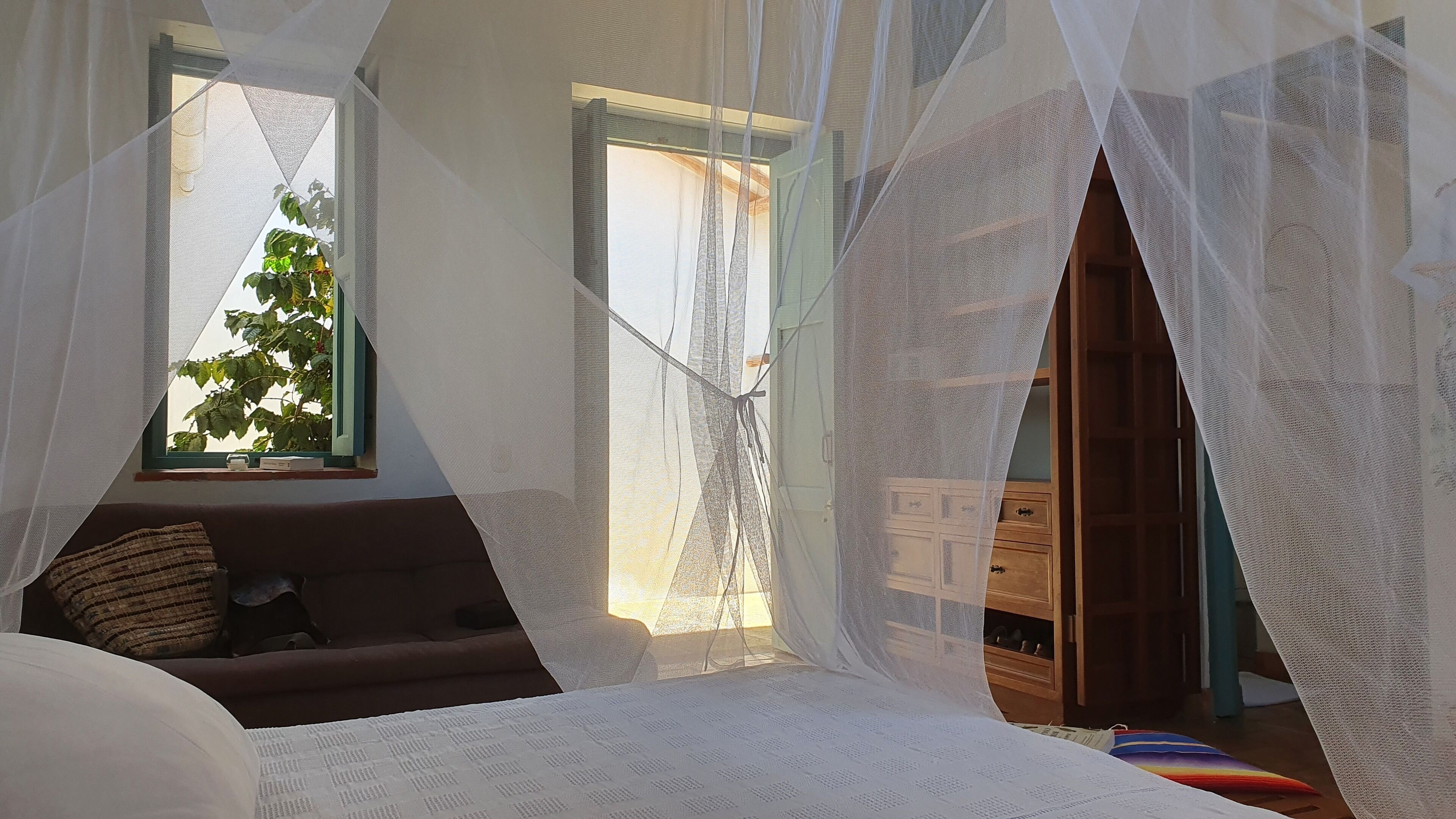 A bedroom with a bed, a window with a view of greenery, and a wooden cabinet.