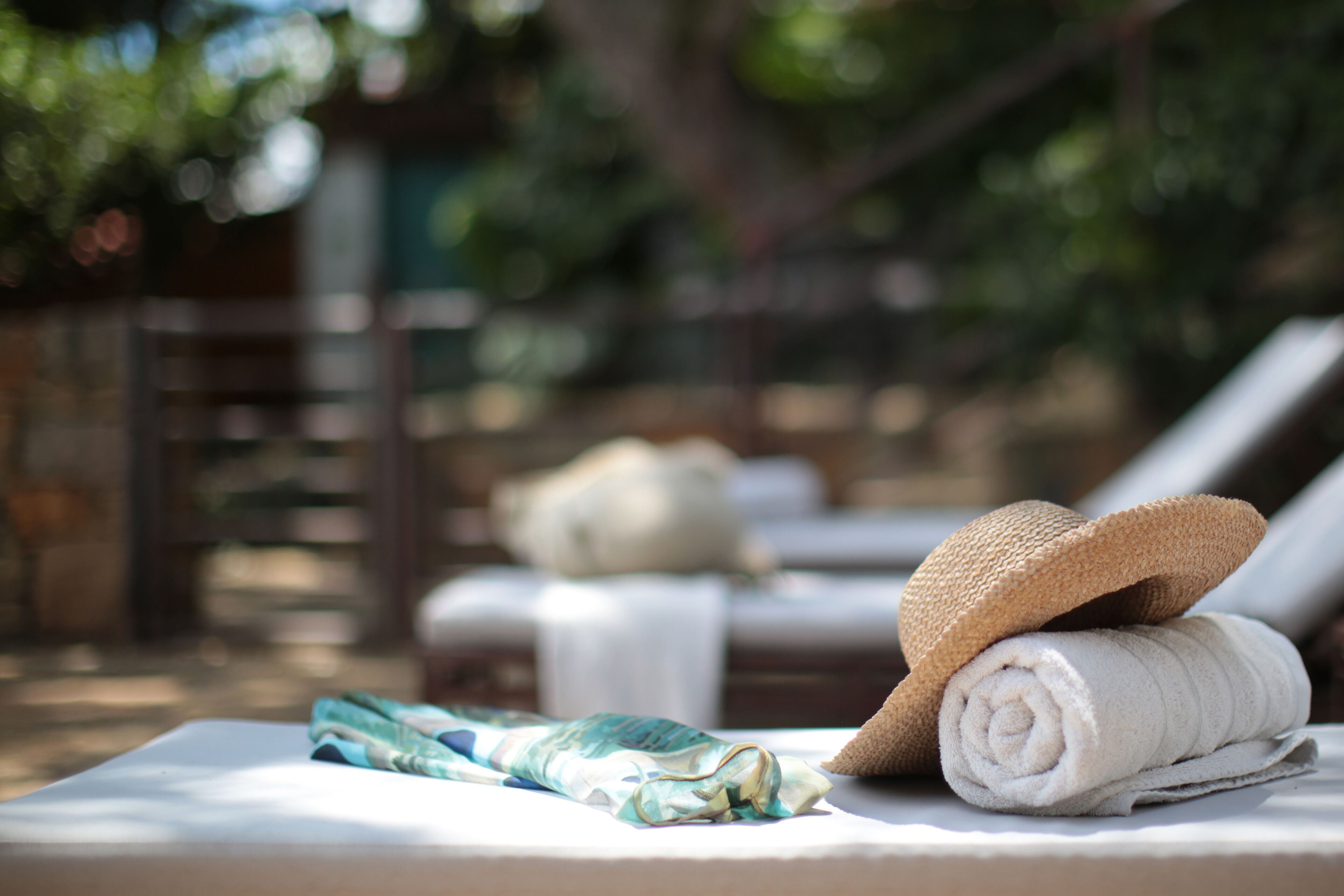 A sun lounger with a rolled towel and a straw hat on it.