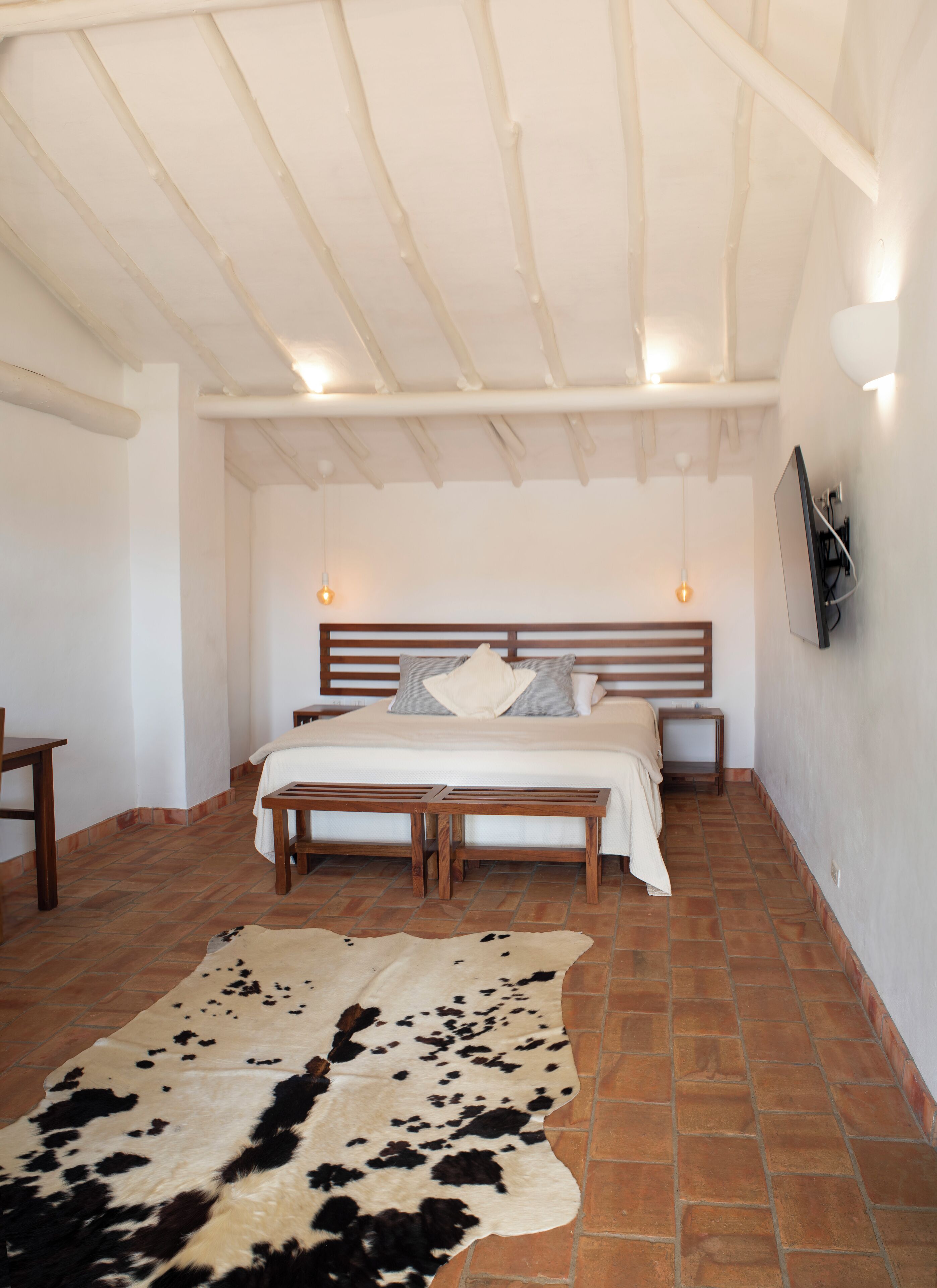A bedroom with a bed, wooden bench, and a cowhide rug.