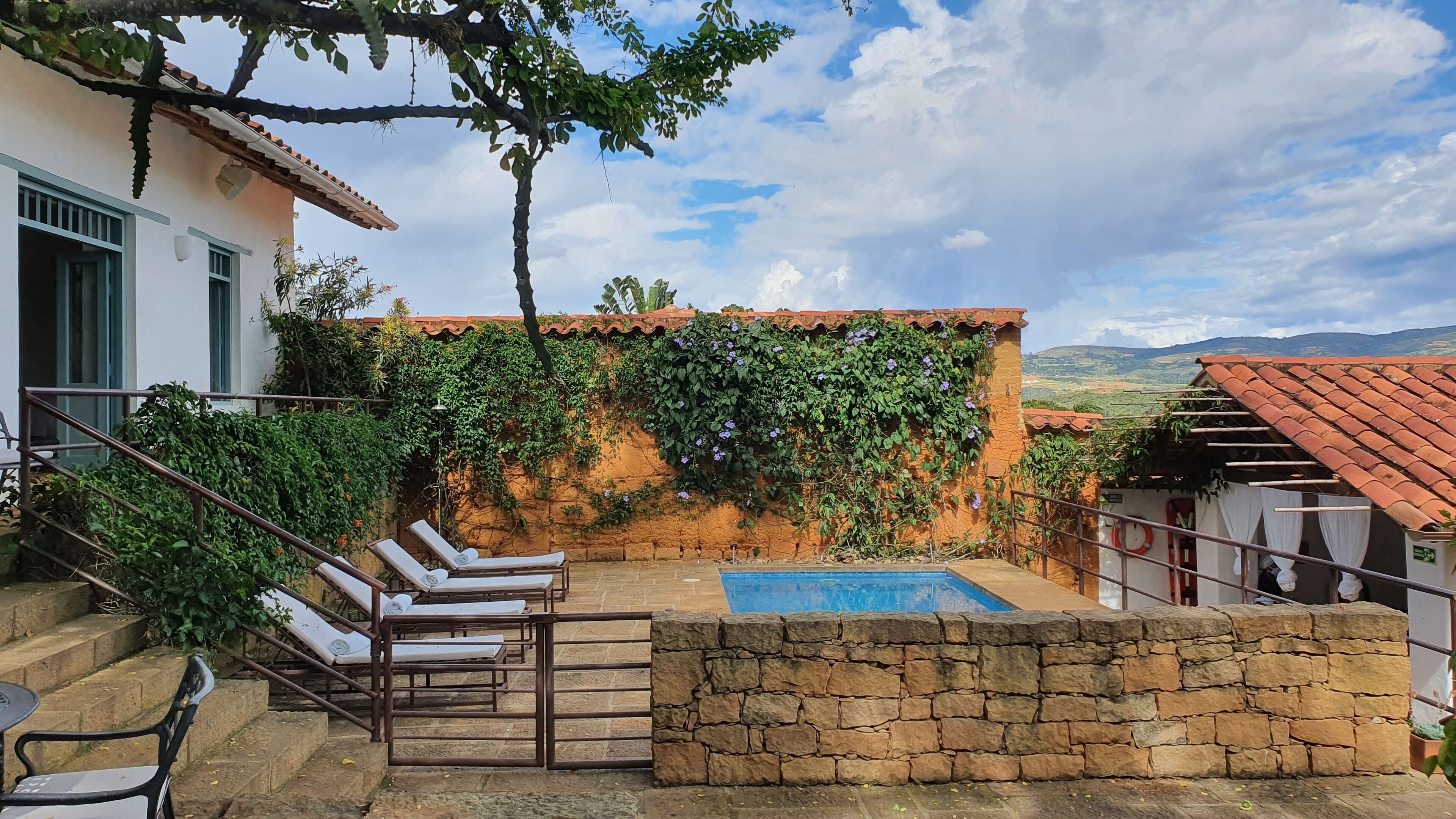A pool area with lounge chairs, a stone wall, and a view of the countryside.
