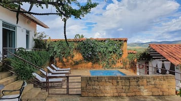 A pool area with lounge chairs, a stone wall, and a view of the countryside.
