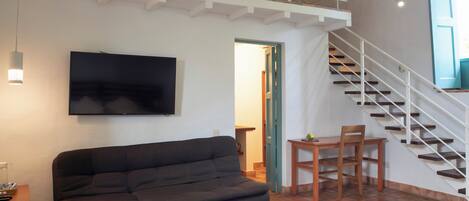 A spacious room with a high ceiling, a large sofa, a wooden table, and a staircase leading to an upper level.