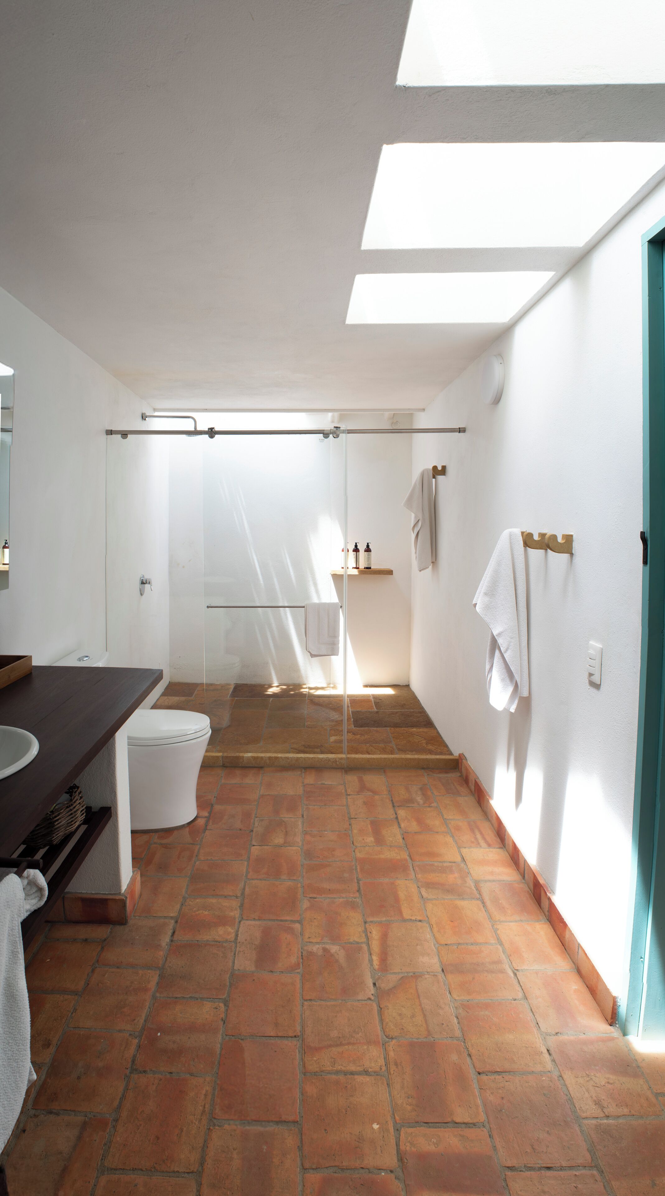 A bathroom with a shower, toilet, and sink. There is a towel rack and a shelf with toiletries.