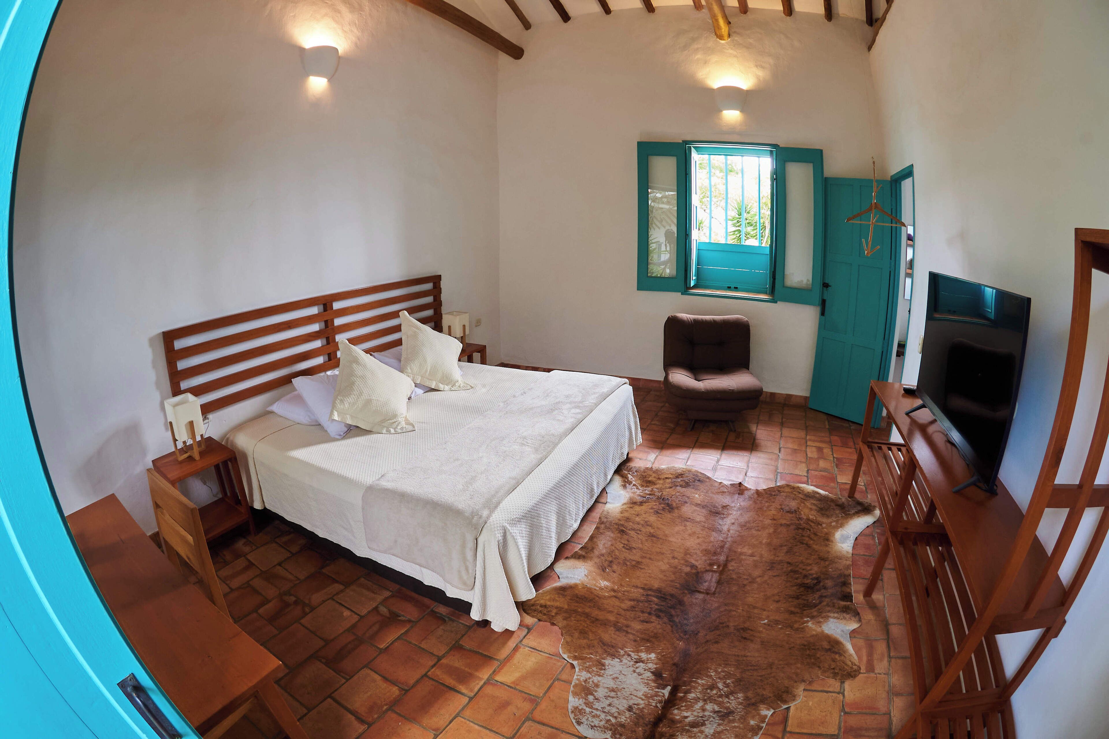A bedroom with a bed, a wooden nightstand, a chair, a television, and a cowhide rug.