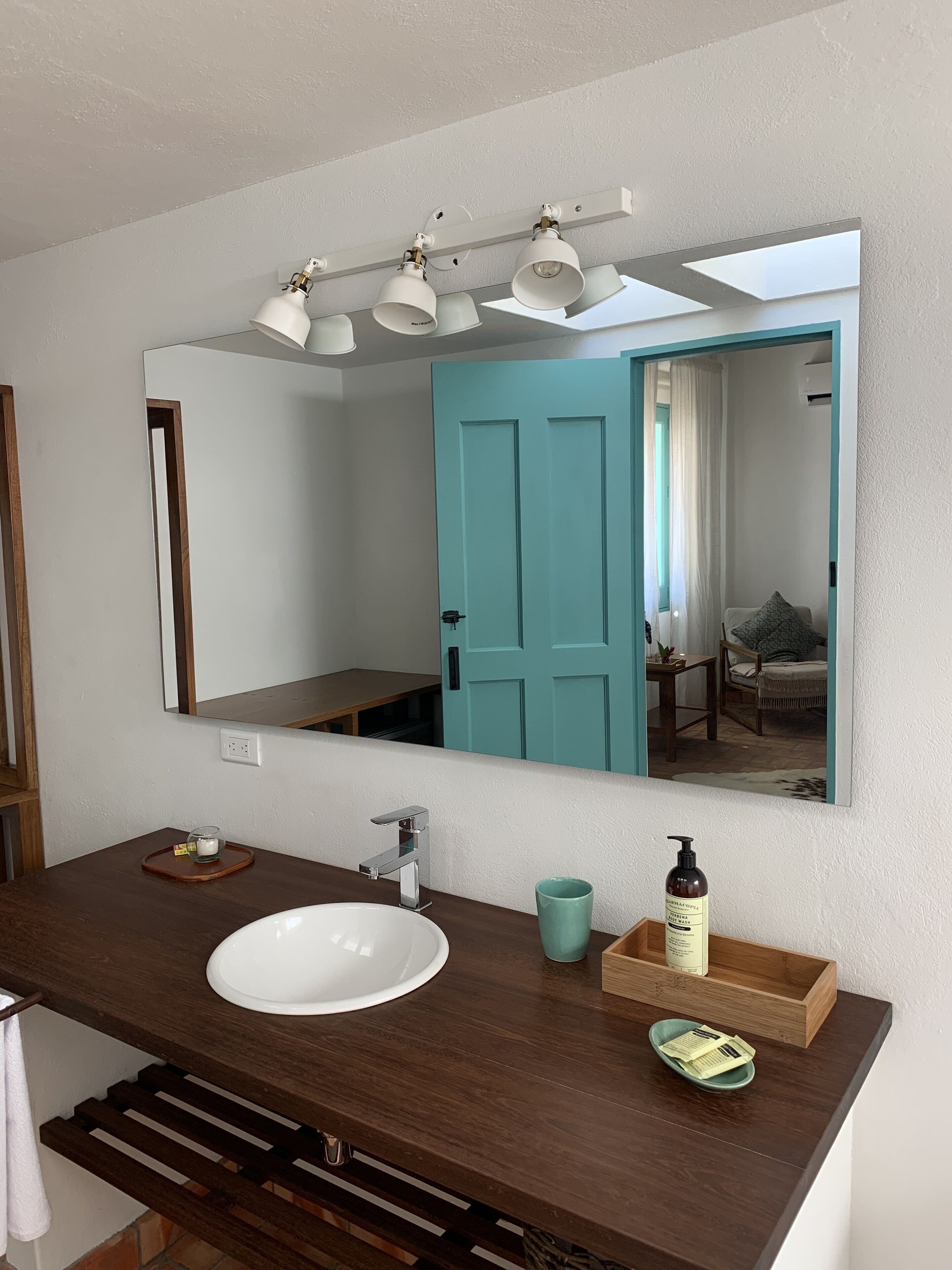 A bathroom with a white sink, a mirror, and a teal door.