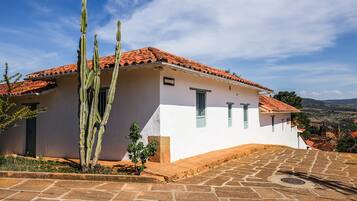 A white building with a red-tiled roof, a cactus in the foreground, and a stone-paved area.