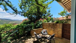 Un patio con una mesa y sillas, rodeado de muros de piedra y abundante vegetación.