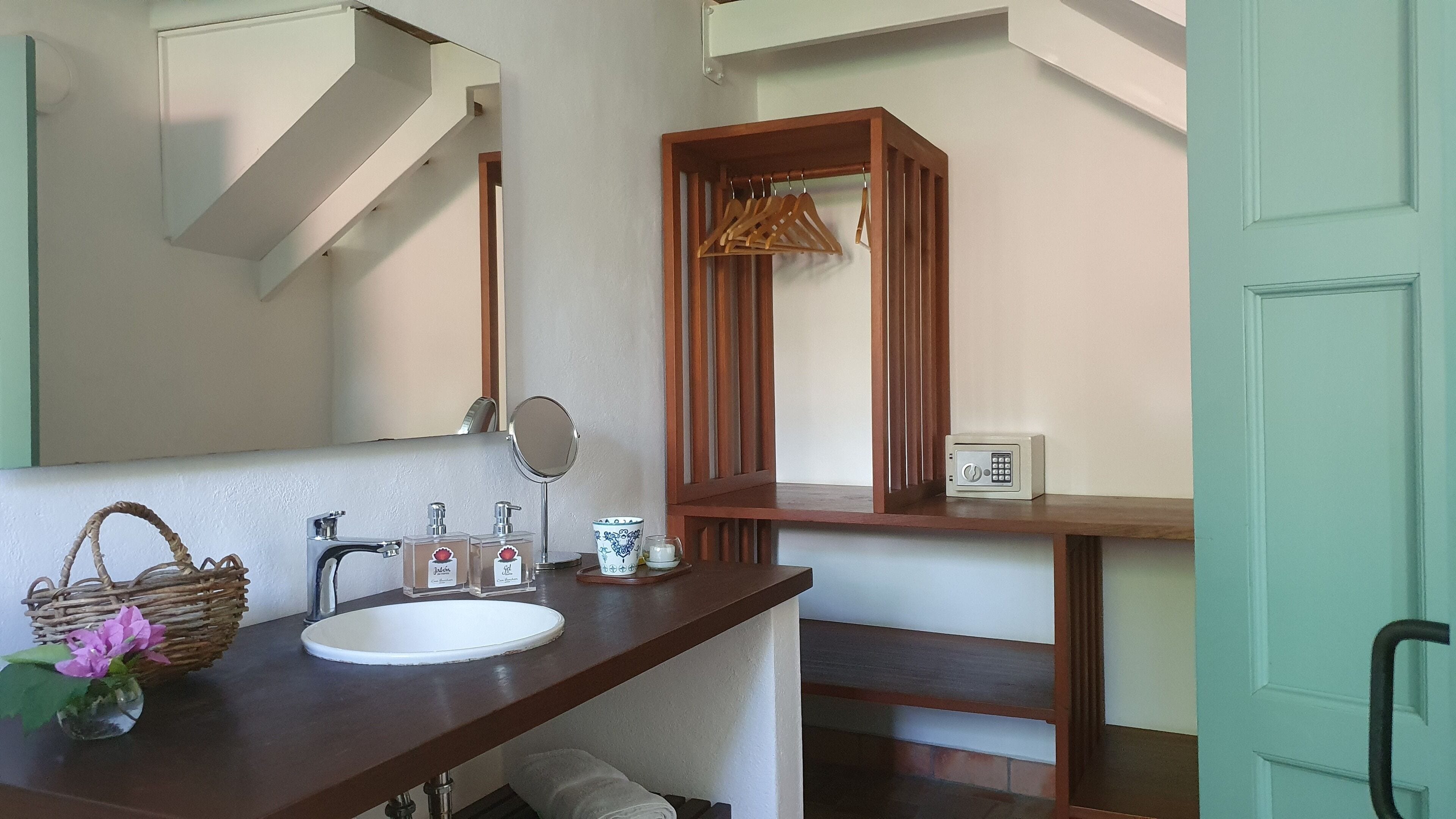 A bathroom with a white sink, wooden vanity, a mirror, a hanging rack, and a small cabinet.