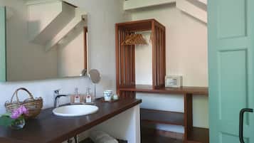 A bathroom with a white sink, wooden vanity, a mirror, a hanging rack, and a small cabinet.