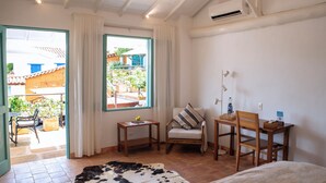 Un dormitorio con una cama, una silla, una mesa, una mesita con un florero y una ventana con cortinas.