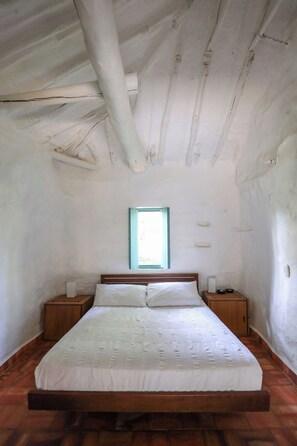 Quarto individual com cama de solteiro, cabeceira de madeira, mesinha de cabeceira e janela com moldura azul.