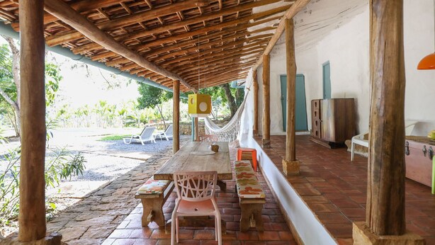 Un espace extérieur abrité, doté de tables et de chaises en bois, d’un hamac et offrant une vue sur la verdure environnante.