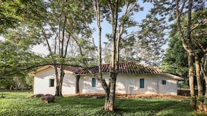 Une maison de campagne au toit de tuiles, entourée d’une végétation luxuriante et d’arbres.