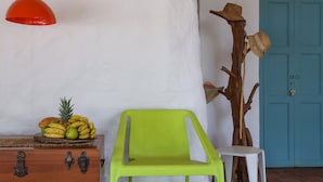 Une pièce comprenant une commode en bois, une chaise en plastique verte, une sculpture d’arbre en bois ornée de chapeaux et une porte bleue.