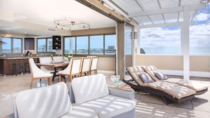 Un vaste espace de vie avec une grande fenêtre donnant sur la mer, un coin repas avec une table et des chaises hautes, et un coin salon confortable avec des fauteuils rembourrés.