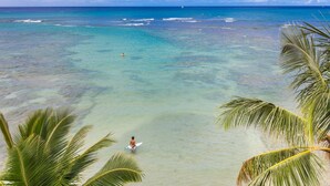 Une plage avec une eau turquoise et limpide, une personne tenant une planche de surf et des palmiers.