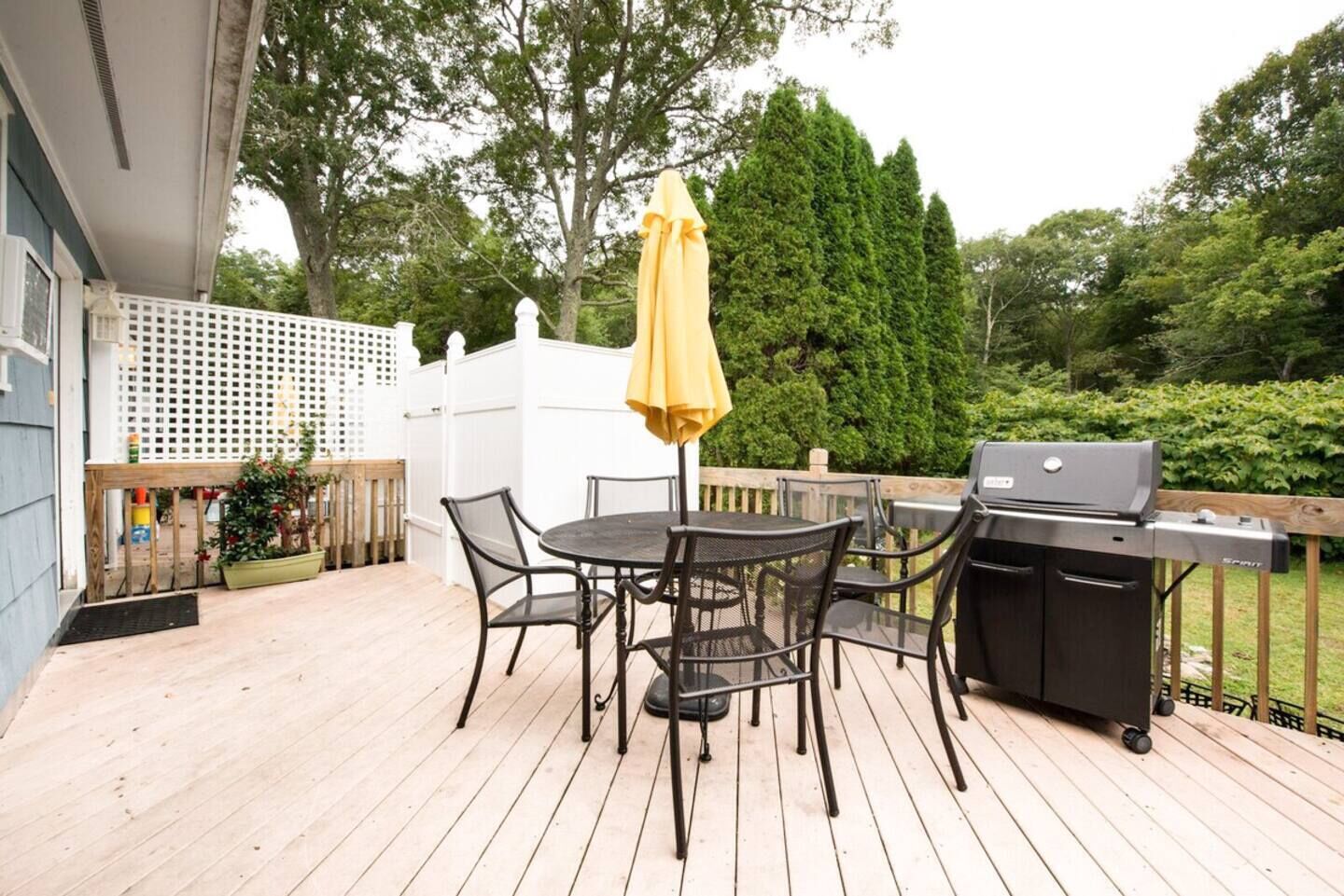 Une terrasse extérieure avec une table ronde et des chaises, un barbecue et un parasol jaune.