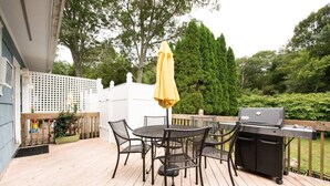 Eine Terrassenausstattung mit rundem Tisch, Stühlen, einem Grill und einem gelben Sonnenschirm.