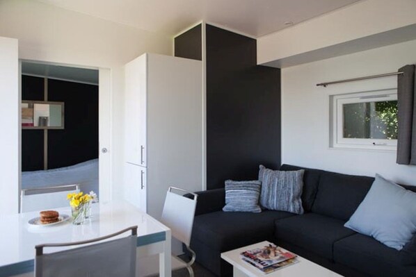 A modern living room with a black sofa, a white coffee table, and a dining area with a white table and chairs.