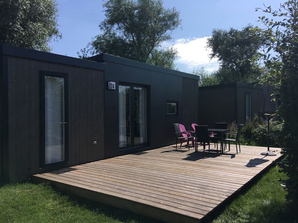 A modern, dark-colored building with a number 24 sign, a deck with outdoor furniture, and a grassy area.