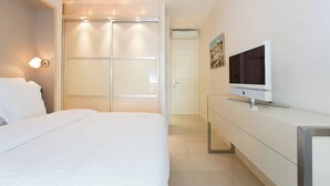 Hotellihuone, jossa on sänky, televisio, vaatekaappi ja liukuovi.