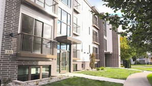 A modern multi-story apartment building with a mix of brick and white exterior walls, large windows, and a well-maintained lawn. - Stunning Downtown Condo: Capri 106 (Traverse City)