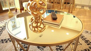 A round glass table with a gold base, a decorative golden object, a book, and a remote control. - Stunning Downtown Condo: Capri 106 (Traverse City)