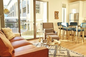 A modern living room with a leather sofa, a round coffee table, and a dining area with blue chairs. - Stunning Downtown Condo: Capri 106 (Traverse City)