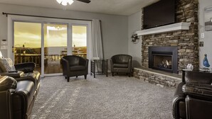 Una sala de estar con chimenea, sofás de cuero, ventilador de techo y vistas a través de puertas de vidrio.