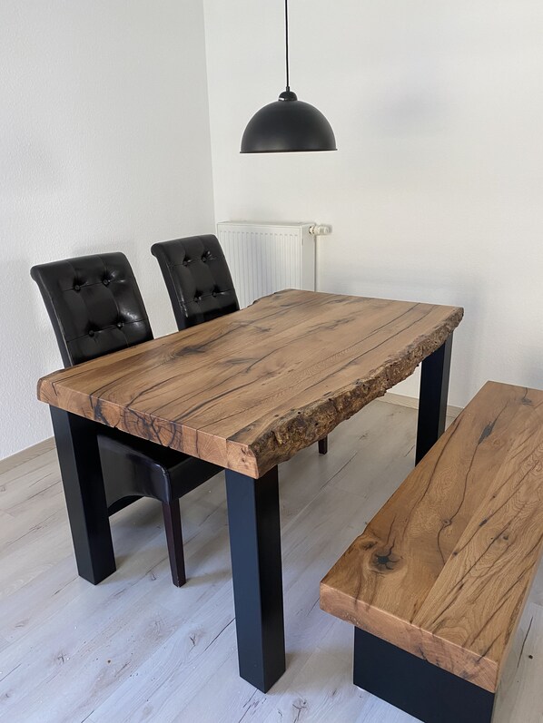 Une table à manger dotée d’un plateau en bois rustique et de pieds en métal noir, accompagnée de deux chaises à revêtement noir.