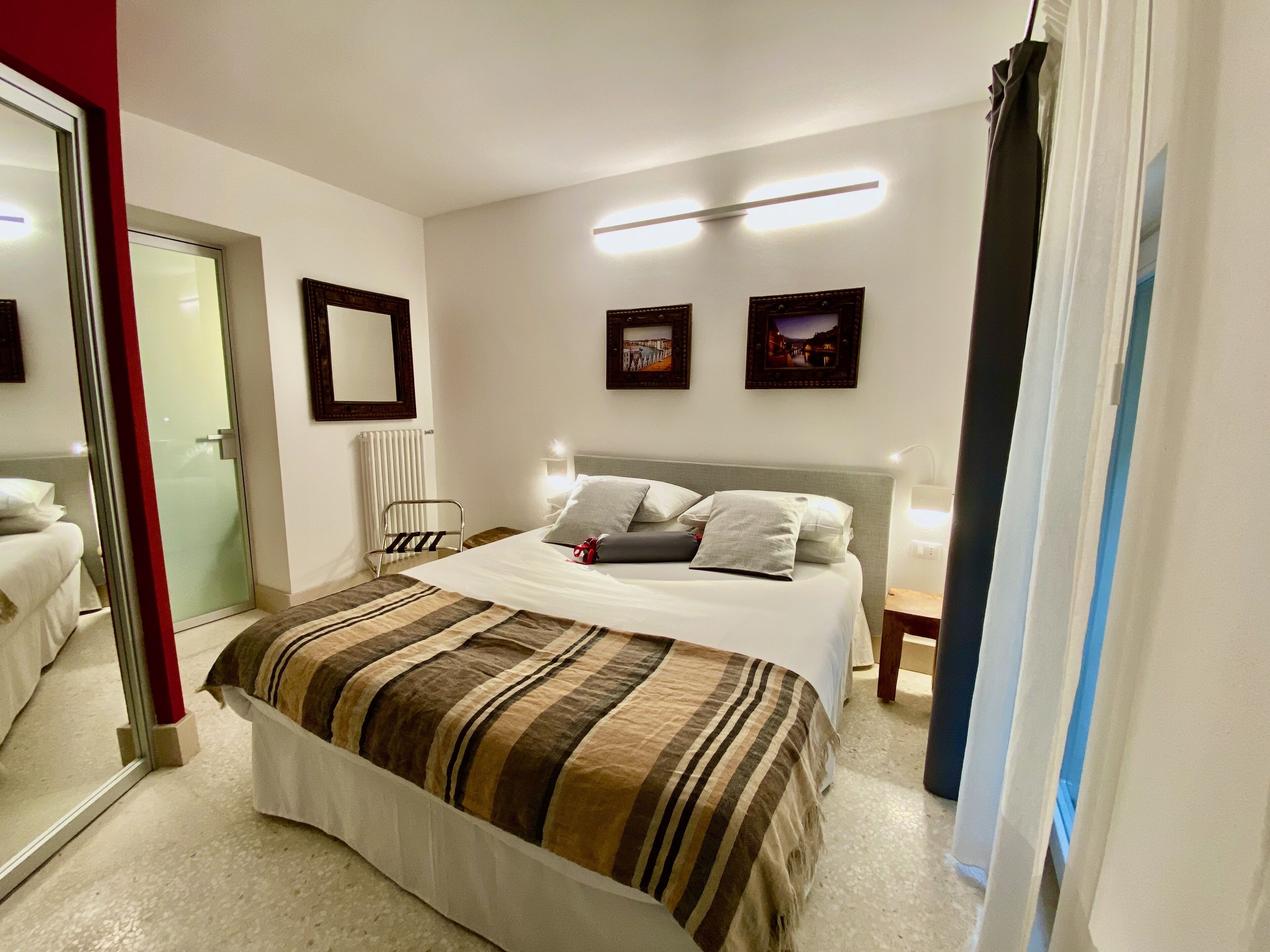 Una habitación de hotel con una cama, una mesita de noche, un espejo y dos cuadros colgados en la pared.
