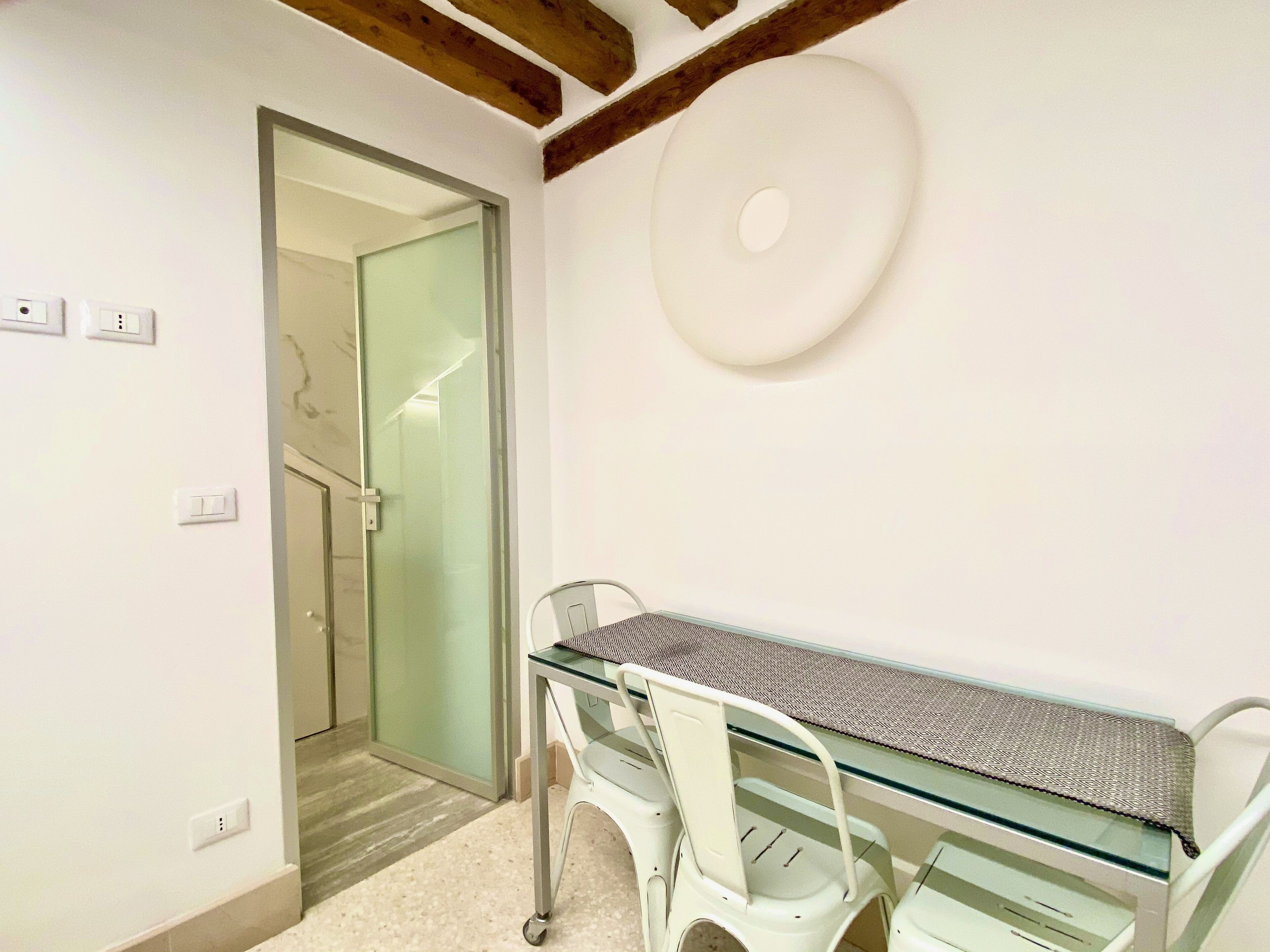 A small, modern room with a glass-top table, white chairs, and a large white wall decoration.