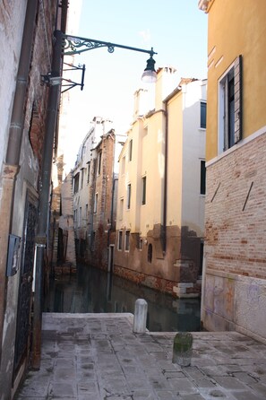 Une ruelle étroite, bordée de bâtiments des deux côtés, avec un canal au milieu et un lampadaire au-dessus.