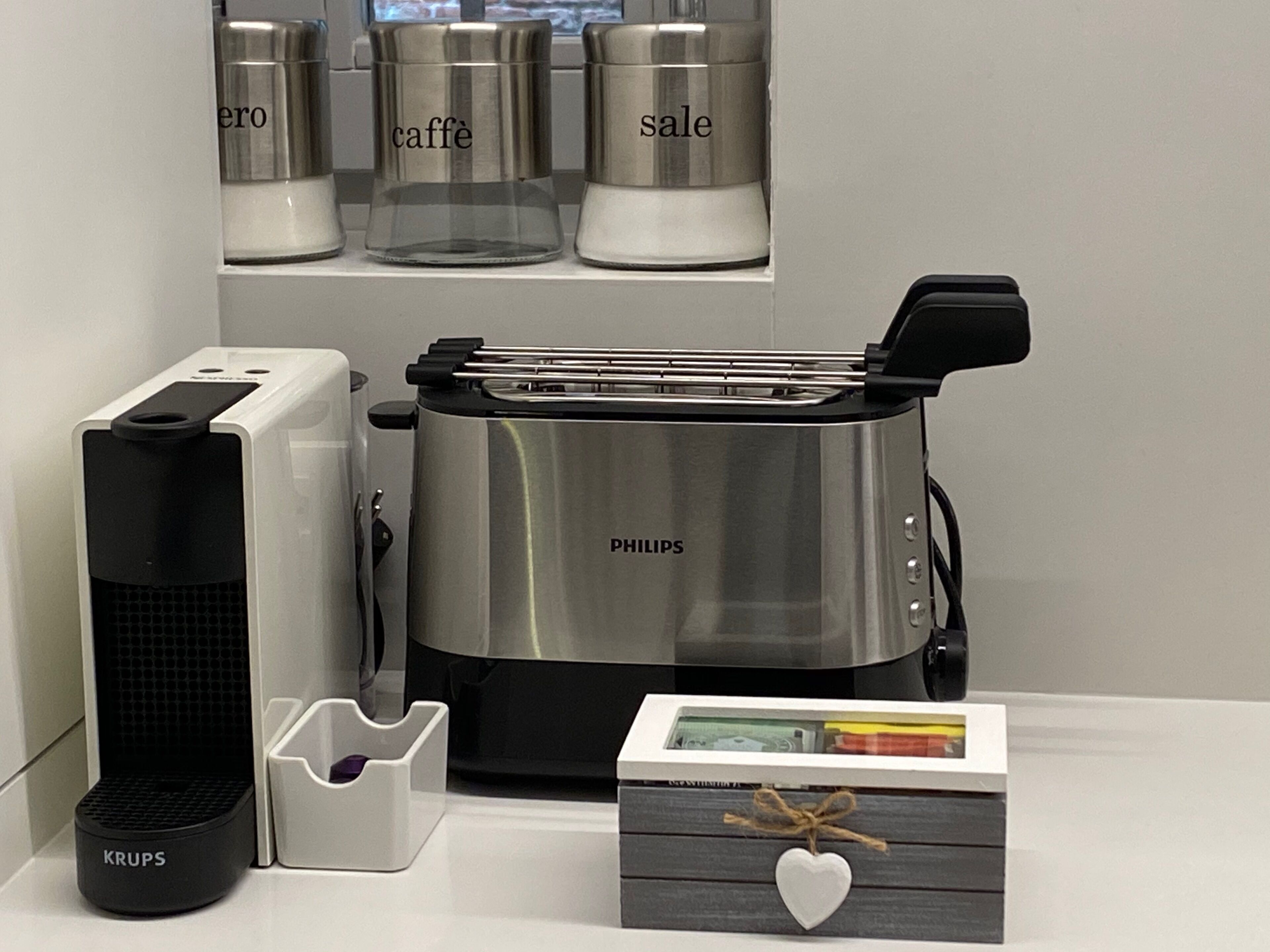 A kitchen with a Philips toaster, a Krups coffee maker, and a box with a heart decoration.