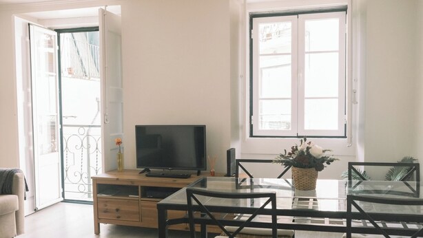 Una sala de estar con televisión, mesa de vidrio, sofá, mueble de madera y balcón con barandilla.