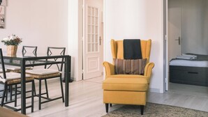 Una habitación con una mesa de comedor, sillas, un sillón amarillo, una cama y una puerta.