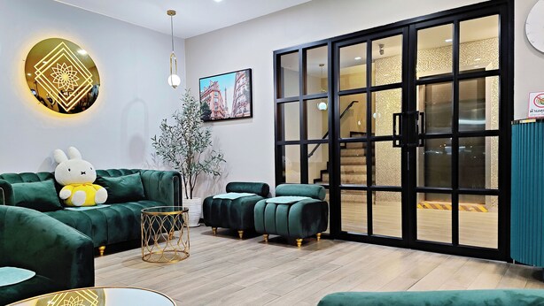 A modern living room with green sofas, a round table, and a large window with a view of the outside. - Koco Hotel (Nakhon Ratchasima)