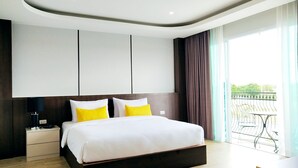 A modern hotel room with a large bed, a nightstand, a desk, and a balcony with a table and chairs. - Koco Hotel (Nakhon Ratchasima)
