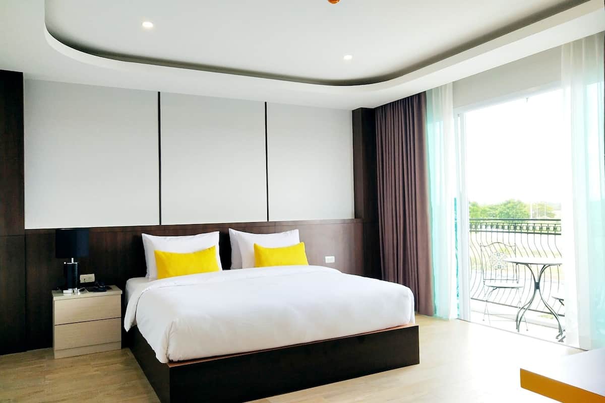 A modern hotel room with a large bed, a nightstand, a desk, and a balcony with a table and chairs.