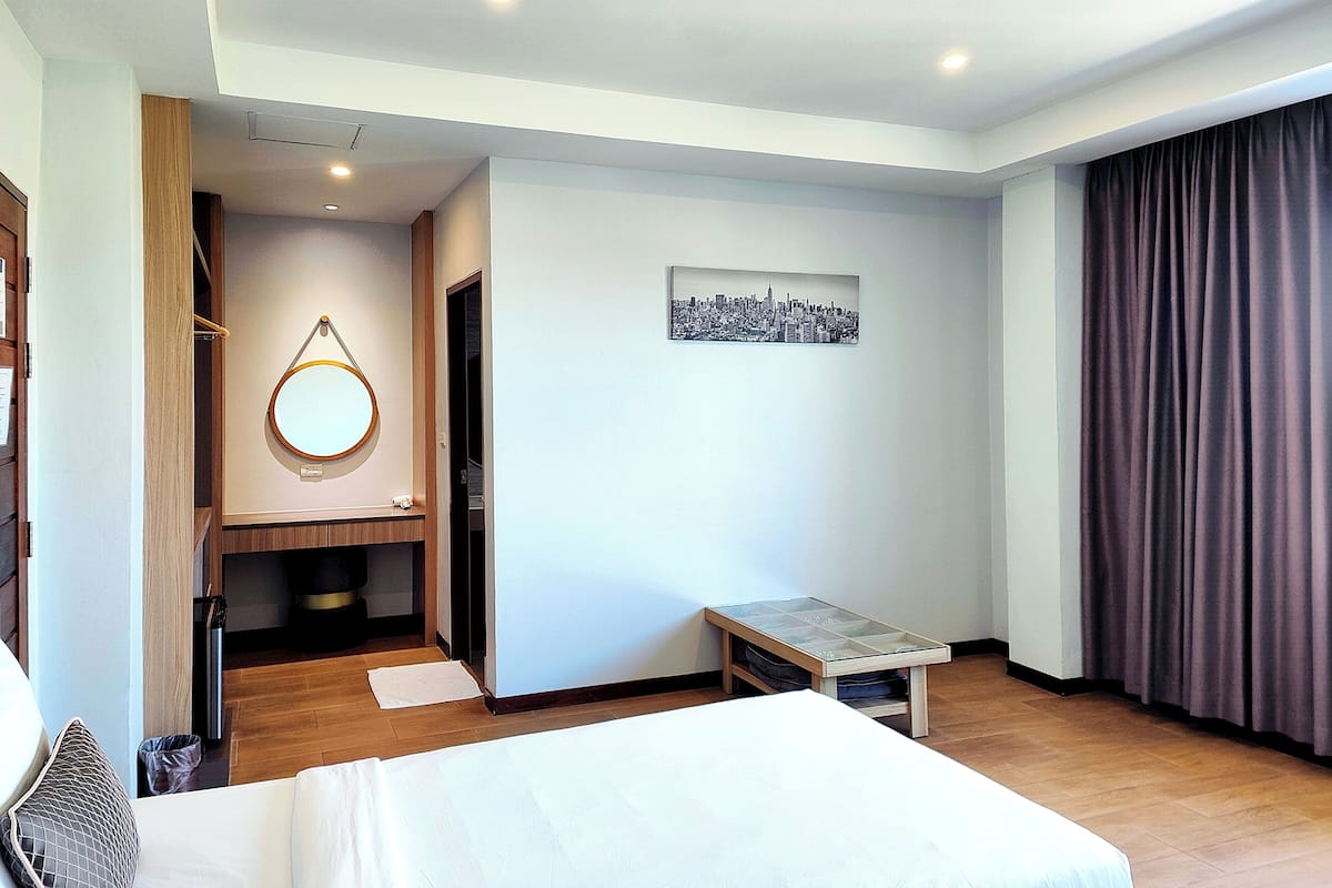 A hotel room with a bed, a bedside table, a mirror, a small table, and a cityscape artwork on the wall.