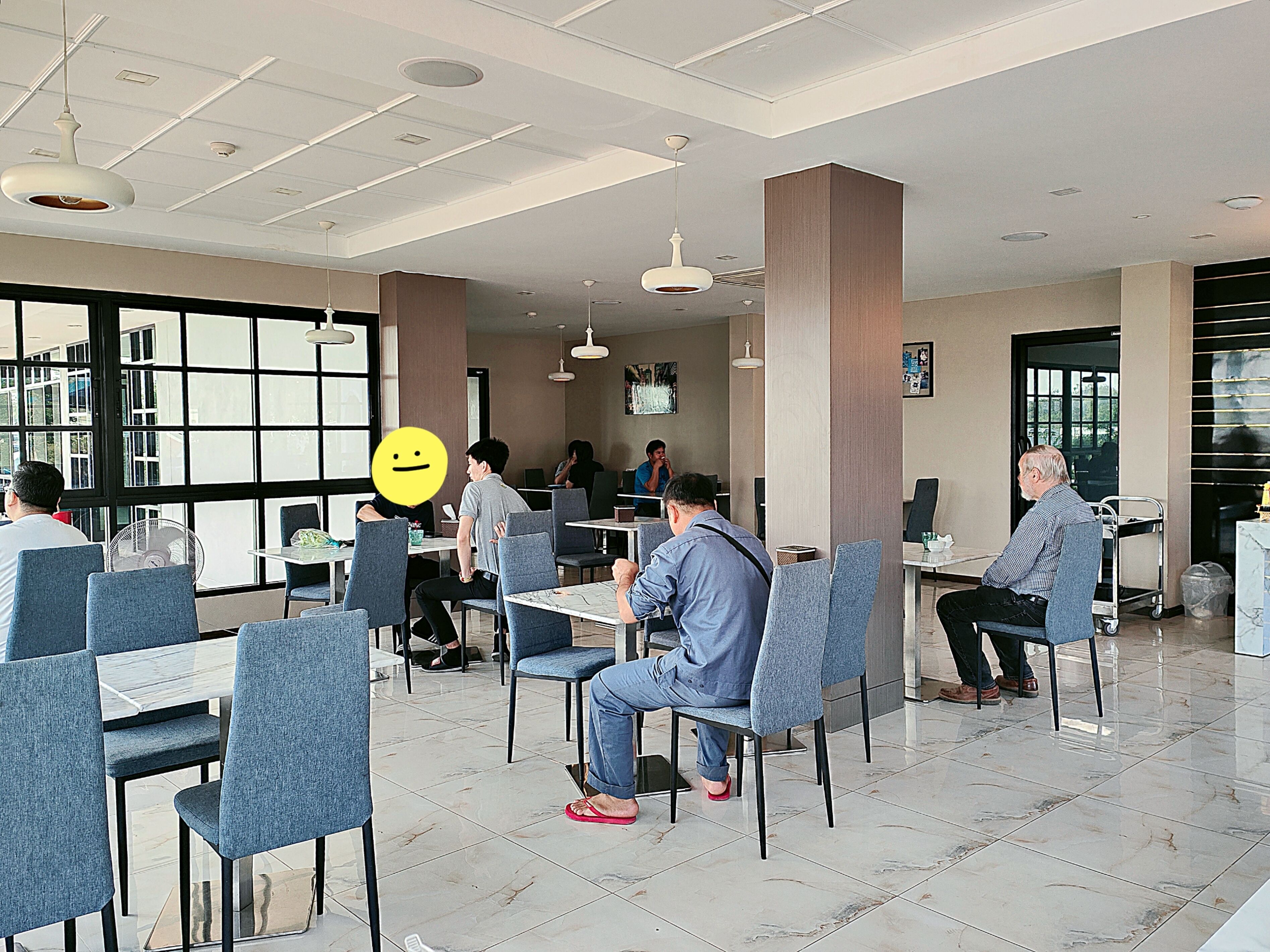 Un comedor moderno con techos altos, ventanas amplias y una variedad de arreglos de asientos, incluyendo mesas y sillas.