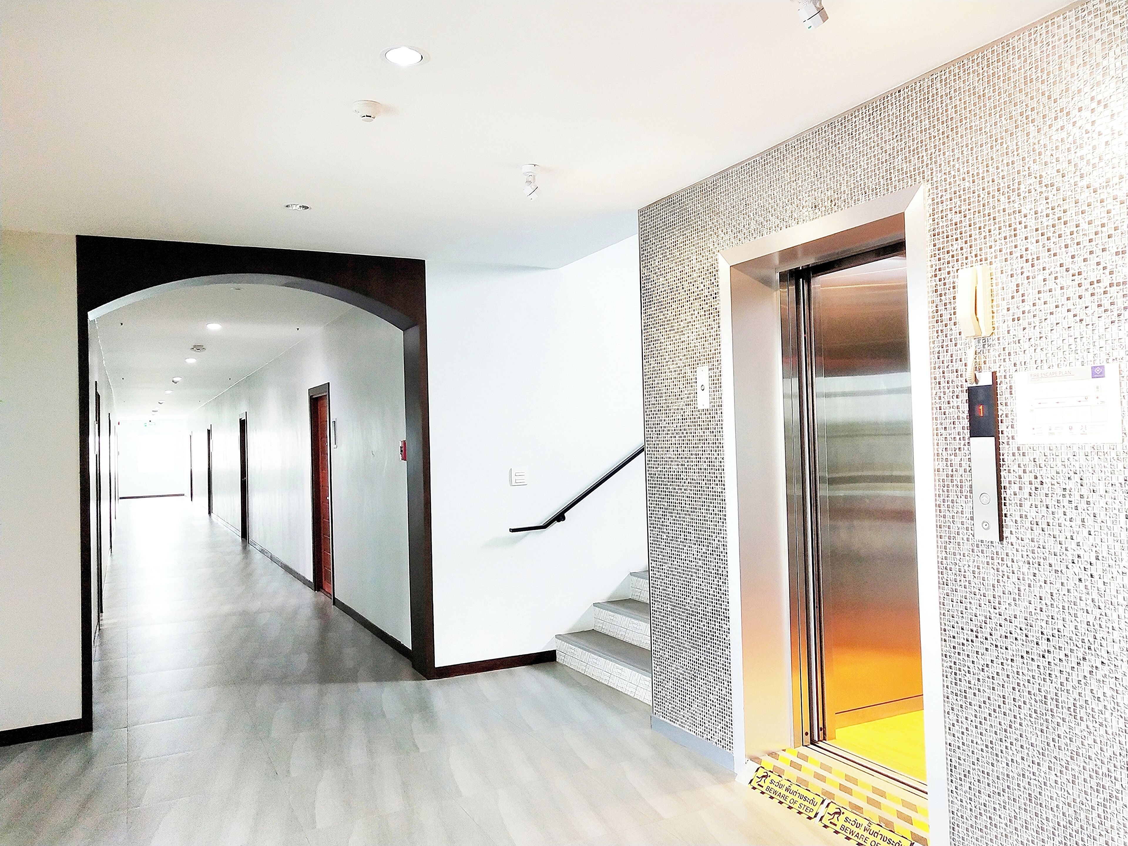 A modern hotel corridor with a wooden floor, a staircase with a patterned wall, and an elevator.