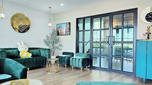 A modern living room with green velvet sofas, a round table, and a large window with a view of the outside. - Koco Hotel (Nakhon Ratchasima)