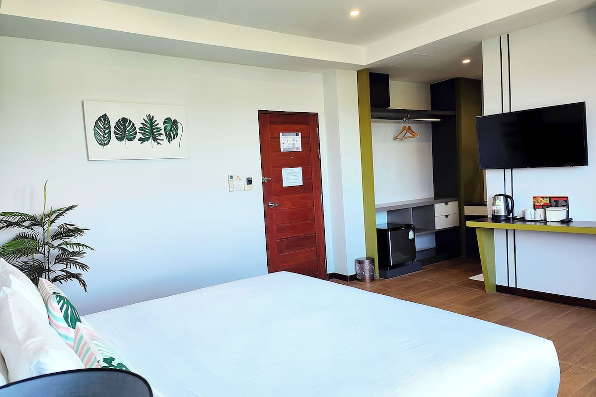 A hotel room with a bed, a TV, a small kitchenette, and a door.