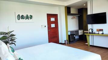 A hotel room with a bed, a TV, a small kitchenette, and a door.