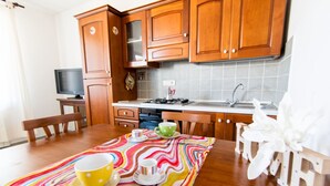 A kitchen with wooden cabinets, a stove, and a sink. There is a dining table with a colorful tablecloth and a few cups and a bowl.