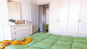 A bedroom with a green bed, a dresser with drawers, a mirror, and a door leading to a bathroom.