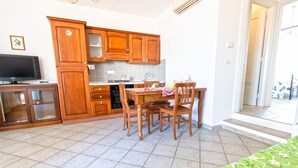 A kitchen with wooden cabinets, a dining table with chairs, a television on a stand, and a tiled floor.